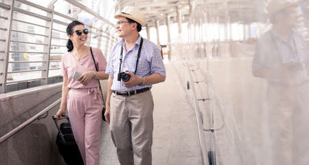 Senior Asian couple with a woman dragging a suitcase and talking happily with smiling at the airport to prepare to travel. Happiness of aunts and uncles in traveling travel together with smile.の写真素材