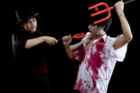Young Asian men in costume hell, evil and wizard with fight on black background with concept for Halloween fashion festival in studio. Two teen Asian man in cosplay Halloween.の写真素材