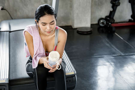 Sexy Asian women hold flask, sit and rest tired on the treadmill after exercise. Fitness in the gym....
