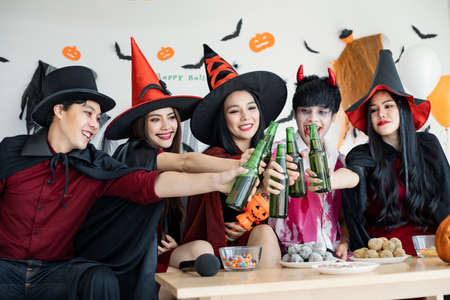 Gang of young Asian in costume witch, wizard with celebrate Halloween party for clink bottle and drink in the room. Group teen Thai with celebrate Halloween. Concept party Halloween at home.の写真素材