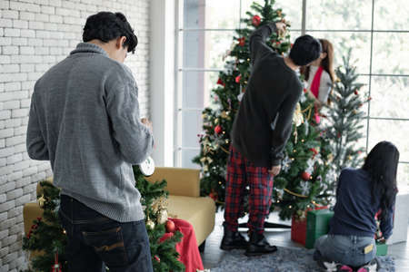 Closeup behind of young man decorating Christmas trees of the Christmas celebration with friends background. Celebrating of new year. Merry Christmas and happy holidays.の写真素材