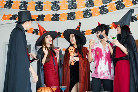 Gang of young Asian in costume witch, wizard with celebrate Halloween party for sing a song and drink, dessert in the room. Group teen Thai with celebrate Halloween. Concept party Halloween at home.の写真素材