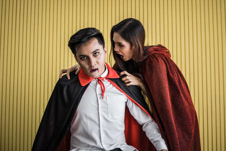 Halloween concept of young Asian woman in costume witch and Asian man in costume dracula on yellow background. Portrait teen couple dressed up as witches and dracula for celebrate  Halloween festival.の写真素材