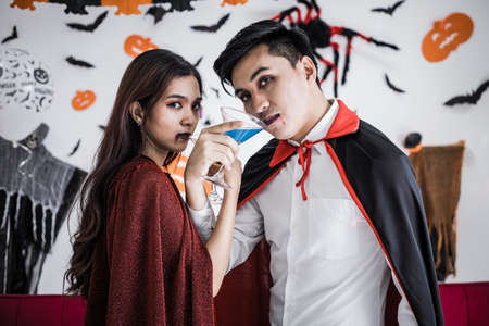 Young Asian couple in costume witch and dracula with celebrate Halloween party and drink wine together in Halloween festival  in the room at home. Concept couple celebrate Halloween together at home.の写真素材