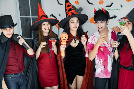 Gang of young Asian in costume witch, wizard with celebrate Halloween party for sing a song and drink, dessert in the room. Group teen Thai with celebrate Halloween. Concept party Halloween at home.の写真素材