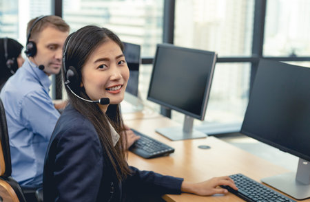 Beautiful Asian woman and group of diverse telemarketing customer service staff team in call center....