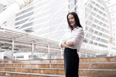 Portrait smile Asian office worker girl with crossed arms at outdoor and copy space. Smiling happy Thai businesswoman with city background.の写真素材