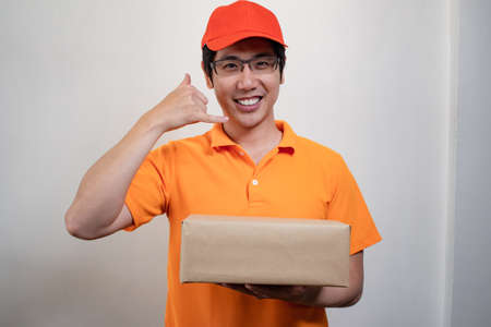 Happy young delivery man in orange dress with parcel post box on white background with smile. Smiling of young male postal delivery courier man in delivering package. Delivery concept.の写真素材