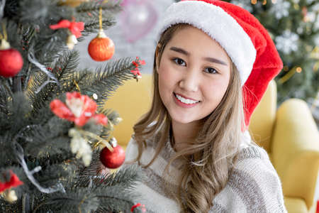 Portrait of young Asian cute woman decorating Christmas trees of the Christmas celebration with smile at home in happy holidays. Happy in Christmas festival and new year.の写真素材