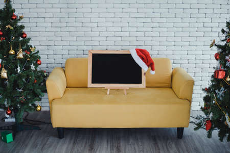 Blackboard for putting text and a red Santa Claus hat, on yellow sofa decorated with Christmas themes in the room at home and copy space. Christmas and happy New Year concept.の写真素材