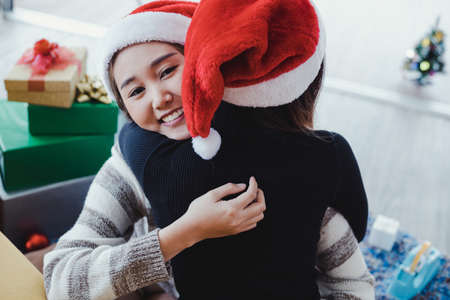Smiling of Asian woman hugs her girl friend with joy after receiving a gift box from her friend at Christmas. Two lovely Thai girls in celebrate Christmas and new year concept.の写真素材