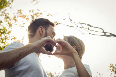 Young lovers kissing stands ready to join hands to form a heart in the park. Teen couples show love to each other in the park. Concept of young couple in the park.の写真素材