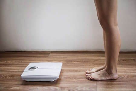 Cropped image of woman feet standing with weigh scales, on wood floor. Overweight problem. Female bare feet standing with a scales.の写真素材