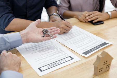 Real estate agent gives the house keys to the client after signing the real estate contract agreement. Successful of couple completes the house purchase contract and the broker gives the house key.の写真素材