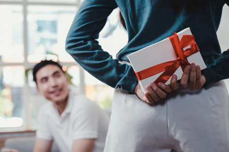 Happy woman surprises her boyfriend by giving a gift box. Young woman surprise  boyfriend with a gift box held on the occasion of the anniversary of love.の写真素材