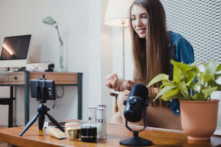 Blogger of caucasian woman with review product and talking camera live recording video on social network at home. Online merchants selling cosmetics on social media via mobile phones.の写真素材