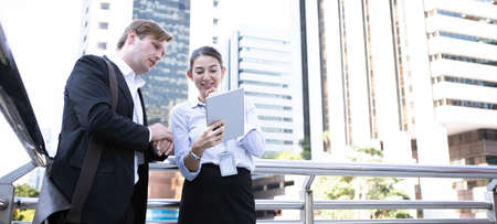 Discussion by tablet of businessman and businesswoman at outside office building.の写真素材