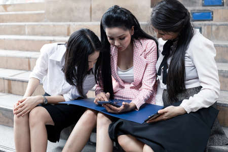 Group of Asian business women sitting on stairs and look at work information in mobile at outdoor. Teamwork Asian women officer concept. Thai women office worker group.の写真素材