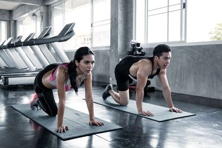 Sexy asian woman workout lower thigh on a yoga mat with trainer man at the gym. Concept of exercise in gym. Woman and man workout on yoga mat.の写真素材