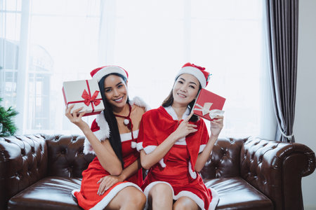 Two Beautiful sexy Asian women santa claus holding gift boxes with happy smile together at home in Christmas festival.の写真素材
