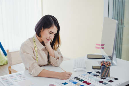 Asian woman designer are thinking and designing clothes for customers order items at the designer desk in the studio. Clothes designers are working in the office. Startup designer concept.の写真素材