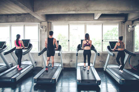 Group of athletes running on electric treadmills at modern gym. People jogging on treadmills.