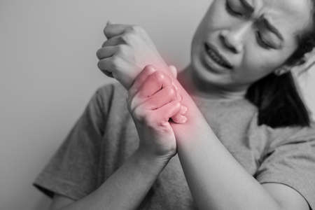 Woman suffering from pain in wrist. Pain in a women wrist. Young woman holding her painful wrist on wall background.の写真素材