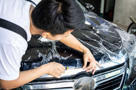Mechanic with transparent film, car paint protection. Mechanic installs car paint protection film. Install car paint protection film. Car wrap concept.の写真素材