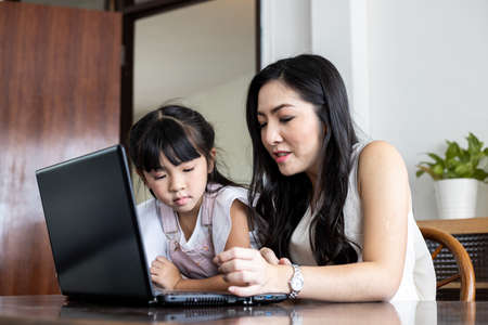 Mother and daughter playing laptop together in the living room at home. Happy loving family concept.の写真素材