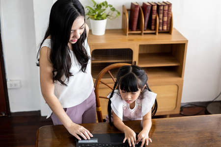Mother and daughter playing laptop together in the living room at home. Happy loving family concept.