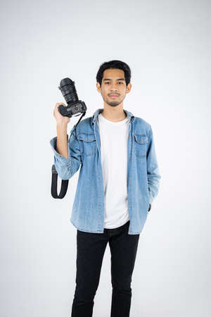 Handsome young photographer poses with smiles and holding professional digital camera in the studio.