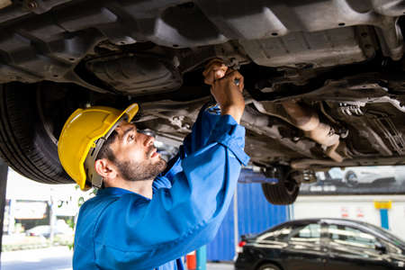 Young mechanic repairing undercarriage of car in auto repair shop.の写真素材
