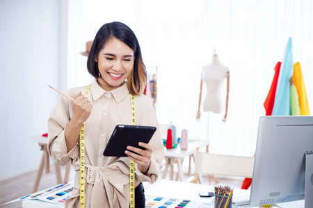 Asian woman designer thinking about designing clothes on a tablet in the studio.