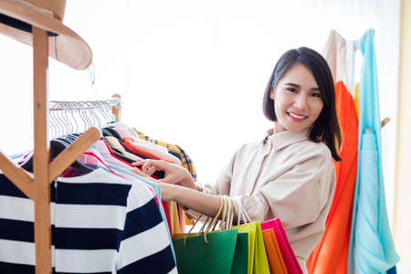 Young woman shopping for clothes hanging on a clothesline with paper bags in department store.の写真素材