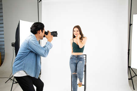 Model young woman posing for photo taken with professional photographer in studio on fashion concept. Photographer and model. Young man photographing fashion model.の写真素材