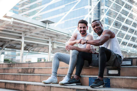 Runner young African American man and caucasian man in sports clothes on the stairs while resting...