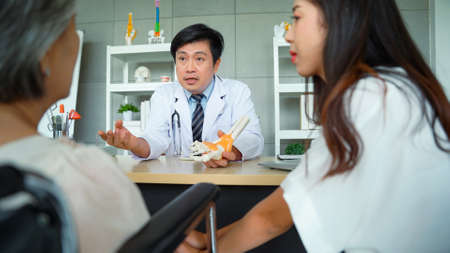 Male doctor explains ankle bone examination results and precautions for elderly female patients and daughters at the hospital.の写真素材