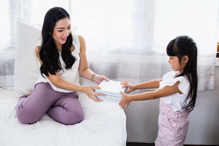 Cute little daughter surprises mom by happily giving a gift box.の写真素材
