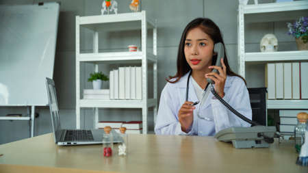 Specialist female doctor talking on the phone ask the patient for the initial symptoms in order to suggest how to fix the initial problem. Female doctor calmly consulting those who ask questions.の写真素材