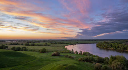 Evening landscape with a river and clouds. Dramatic sunset over the river. Bright green grass and colorful sunset.の写真素材
