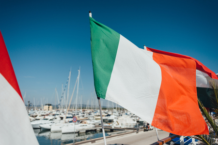 Italian flag over yacht parking in harbor, harbor yacht club in Marina di Scarlino, Italy. Italian flag in blue sky backgroundの写真素材