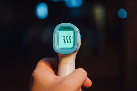 Contactless Infrared thermometer on dark background. Temperature measurement in a public placeの写真素材