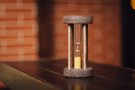 Vintage wooden hourglass against brick wall background. Time is running outの写真素材