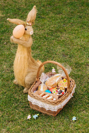 Easter basket with ukrainian easter cake, cookies and Easter eggs on green lawn. easter bunny figureの写真素材