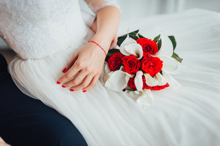 Close-up of bride's hands and a red and white wedding bouquetの写真素材