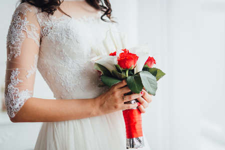 Close-up of bride's hands holding rich red and white wedding bouquetの写真素材