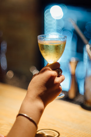 Female hand holding a glass of white wine on the background of the barの写真素材