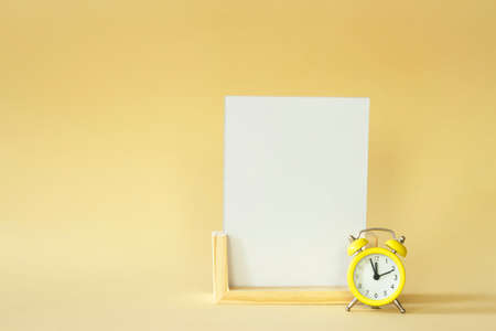 A white sheet with space for text and a vintage clock on a yellow background.の写真素材