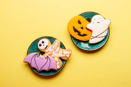 Homemade cookies cute skeletons, ghosts, bats and pumpkins for Halloween on a plate on a yellow...