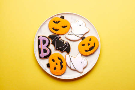 Homemade cookies cute skeletons, ghosts, bats and pumpkins for Halloween on a plate on a yellow...